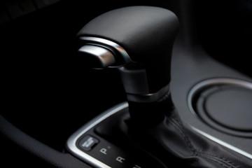 Car interior. Black leather automatic gearbox with chrome button and blurred round ashtray on background