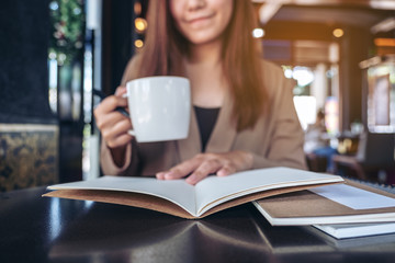 Closeup image of an asian woman reading and opening a book while drinking coffee in cafe