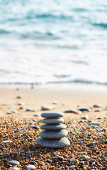 Fototapeta na wymiar Zen pyramid of spa stones on the blurred sea background. Sand on a beach. Sea shores. Water waves texture. Central side of photo. Place for text. Vertical