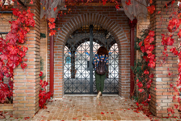 Girl looking inside from Decorative arched iron gateway through brick door to a garden with...