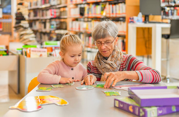 Granddaughter and grandmother put together a puzzle in the city library