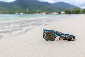 Old sunglasses overgrown with algae and shells on the white sand of a tropical beach