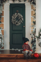 Cute child boy sits on the porch of the magic house of Santa Claus. Miracle time. Merry Christmas and Happy New Year