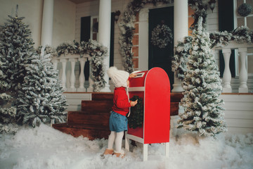 A little baby girl in a white knitted hat makes a wish and writes a letter to Santa Claus and sends...