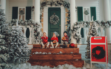 A portrait of children sitting on the porch of their house together, Eat bagels. Merry Christmas, happy New Year. Yard with a christmas tree, lights and decorations. Miracle time.
