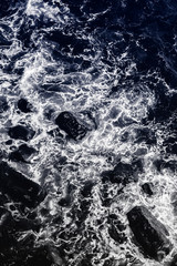 Water and rocks (duotone) . Small waves crash on a rocky shoreline and create whirlwinds of white foam, seen from above