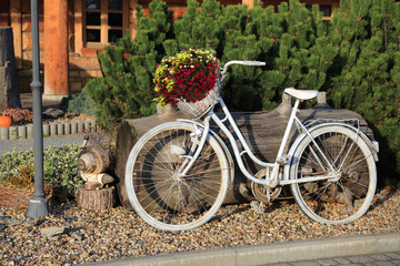 Stary, biały rower z koszykiem kwiatów przed restauracją.