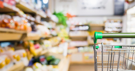supermarket shopping cart with abstract blur organic fresh fruits and vegetable on shelves in grocery store