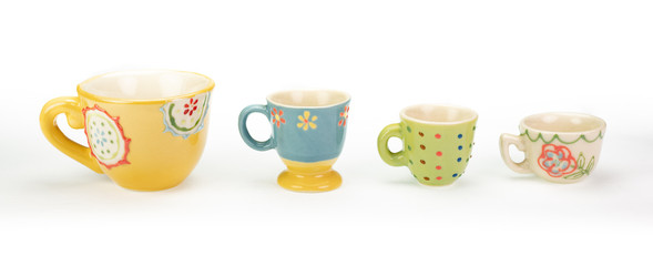 Four pretty ceramic teacups in a row on white background. Varying colours, patterns and sizes in descending order. Cheerful bright pastel colours. In a banner shape.