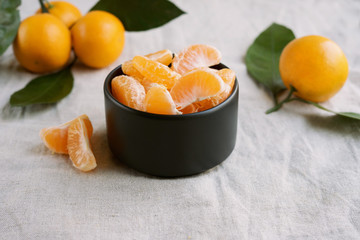 Peeled mandarine in black bowl on linen tablecloth