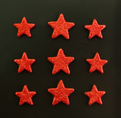 Fototapeta na wymiar Nine red stars on black background. Flat lay. View from above