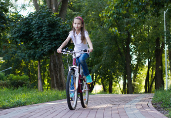 Cute girl riding her bike in the park in the sun.