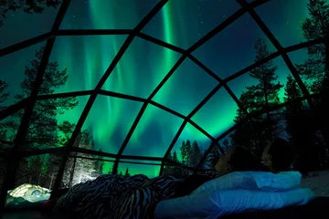 Foto auf Alu-Dibond NAHAUFNAHME Junges kaukasisches Touristenpaar, das den Nachthimmel von einem kühlen Glashaus in der skandinavischen Wildnis aus beobachtet. Freundin und Freund genießen einen romantischen Abend in einem coolen Glasiglu. © helivideo