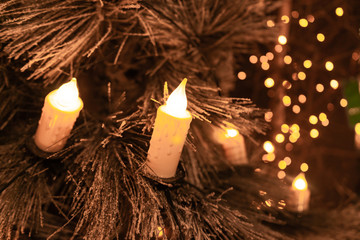 Traditional candles on flocked Christmas tree with glowing lights background