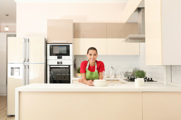 Beautiful young woman with clean dishes in kitchen