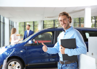 Fototapeta premium Salesman with clipboard near new car in modern auto dealership