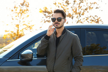 Young man talking on phone near modern car, outdoors