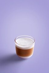 Small cappuccino coffee in transparent mug on a purple background