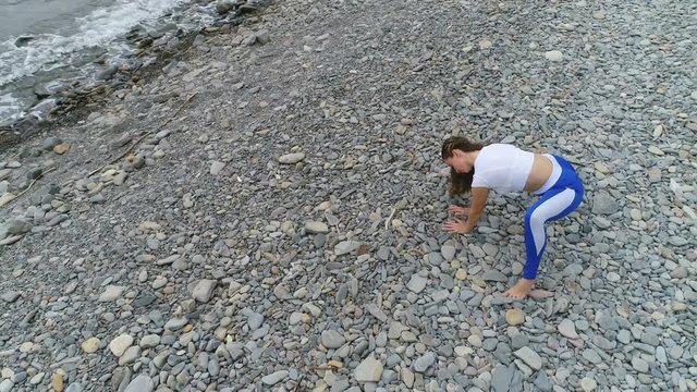 Woman is doing yoga and stretcing exercises on rock and sea background. Aerial beautiful footage view.