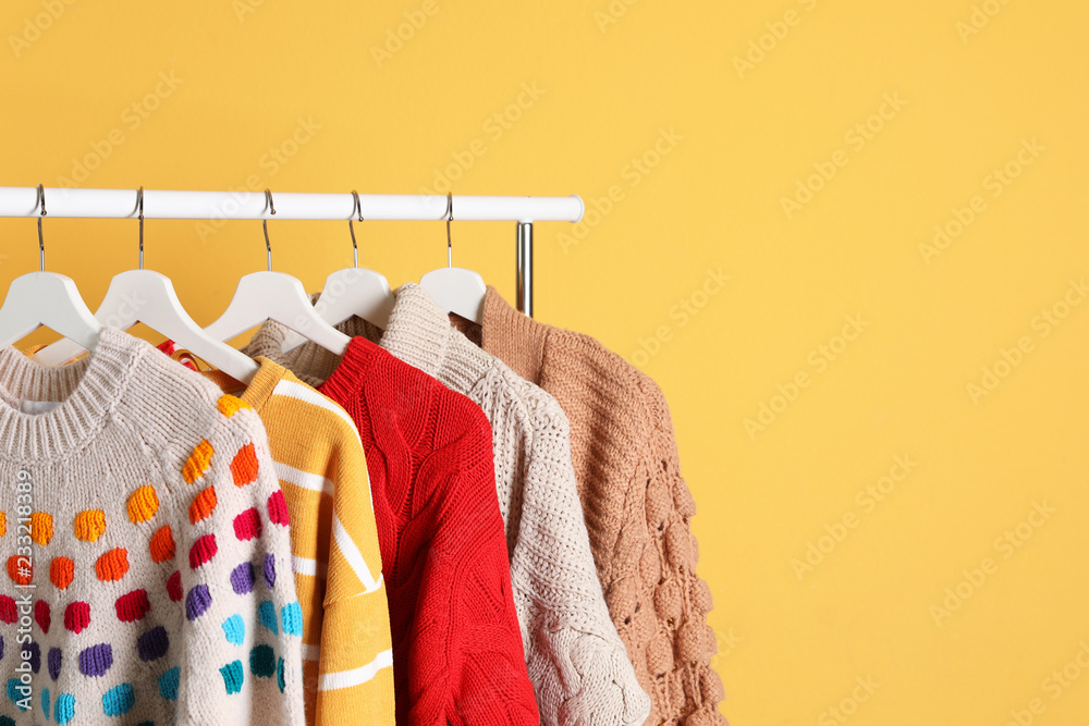 Wall mural Collection of warm sweaters hanging on rack against color background. Space for text