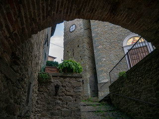 View of a church from an arch of an old narrow alley in a small Italian village in the mountains of Tuscany, Italy, in the sun after rain
