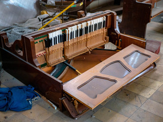 Old broken piano fallen over and destroyed by vandalism in an abandoned church, forgotten and left behind between piles of trash