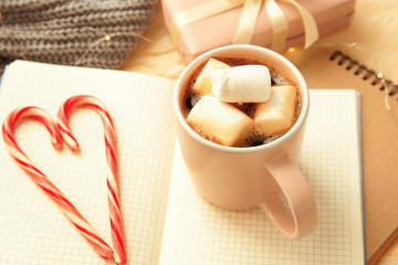 Hot winter drink in cup and candy canes on notebooks. Cozy season