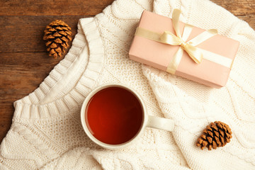 Flat lay composition with cup of hot winter drink and warm knitted sweater on wooden background. Cozy season