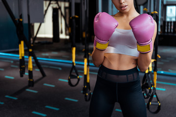 Fototapeta na wymiar Partial view of female boxer in pink boxing gloves practicing boxing in gym