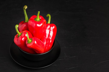 Red peppers in plate on black background - closeup photo of whole fresh ripe sweet vegetables in dark mood style.