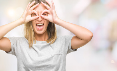 Young beautiful woman over isolated background doing ok gesture like binoculars sticking tongue out, eyes looking through fingers. Crazy expression.