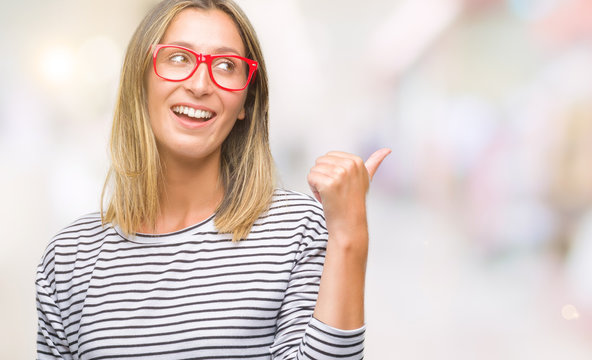 Young beautiful woman wearing glasses over isolated background smiling with happy face looking and pointing to the side with thumb up.