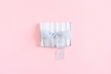 Gift box with blue ribbon bow on a pink pastel background