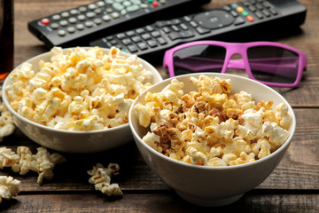 Popcorn, 3D glasses and TV remote on a brown wooden background. concept of watching movies at home.