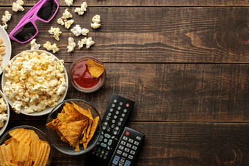 Popcorn and various snacks, 3D glasses, TV remote on a brown wooden background. concept of watching...