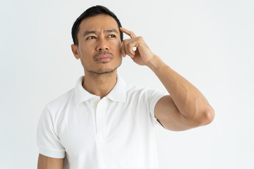 Pensive young businessman thinking over business project. Handsome Latin man scratching head and...