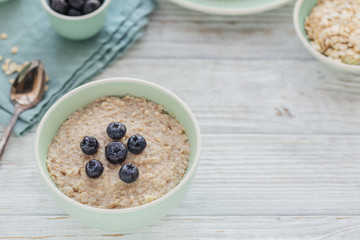 Oatmeal porridge bowl on the white wooden background.