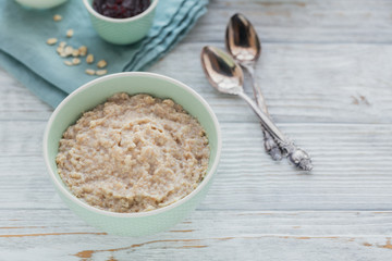Oatmeal porridge bowl on the white wooden background.