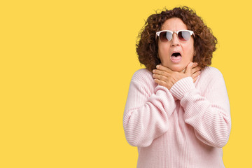 Beautiful middle ager senior woman wearing pink sweater and sunglasses over isolated background shouting and suffocate because painful strangle. Health problem. Asphyxiate and suicide concept.