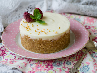 Cheesecake with raspberries and mint on a pink plate on a wooden table with floral fabric and laces. Close up, copy space, selective focus