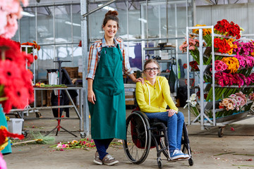 Female Worker Standing By Disabled Colleague In Greenhouse