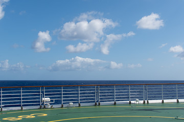 View from the ship to the ocean with clouds over the horizon and part of the helipad and fence in the foreground.