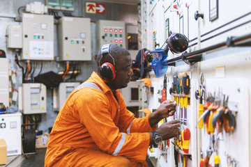 African marine engineer officer in engine control room ECR. He works in workshop and chooses...