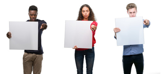 Composition of young people holding blank banner over isolated background pointing with finger to the camera and to you, hand sign, positive and confident gesture from the front