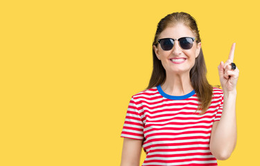 Fototapeta premium Middle age mature woman wearing sunglasses over isolated background pointing finger up with successful idea. Exited and happy. Number one.