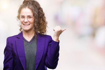Young brunette student girl wearing school uniform and glasses over isolated background smiling with happy face looking and pointing to the side with thumb up.