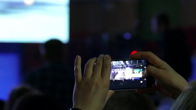 Shoots video of the concert on the smartphone. Performance on stage.