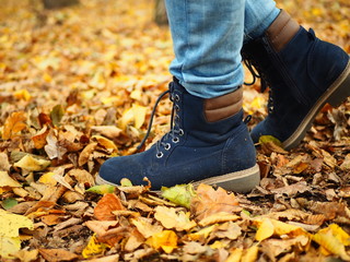 Closeup of child legs in navy shoes on bright autumn leaves background. The teenager walks in the park. Maple leaves of different colors, yellow, orange, green.
