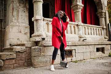 Fototapeta na wymiar Stylish african american woman in red coat posed against old columns.