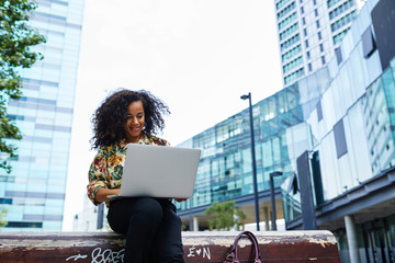Happy businesswoman browsing laptop in city centre.